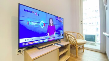 A television displaying a news channel, a wooden entertainment unit, and a wicker chair.