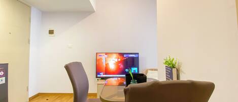 A room with a television on a stand, a chair, a small table, and a potted plant.