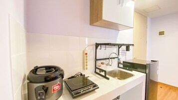 A compact kitchen with a microwave, a rice cooker, a kettle, and a sink.