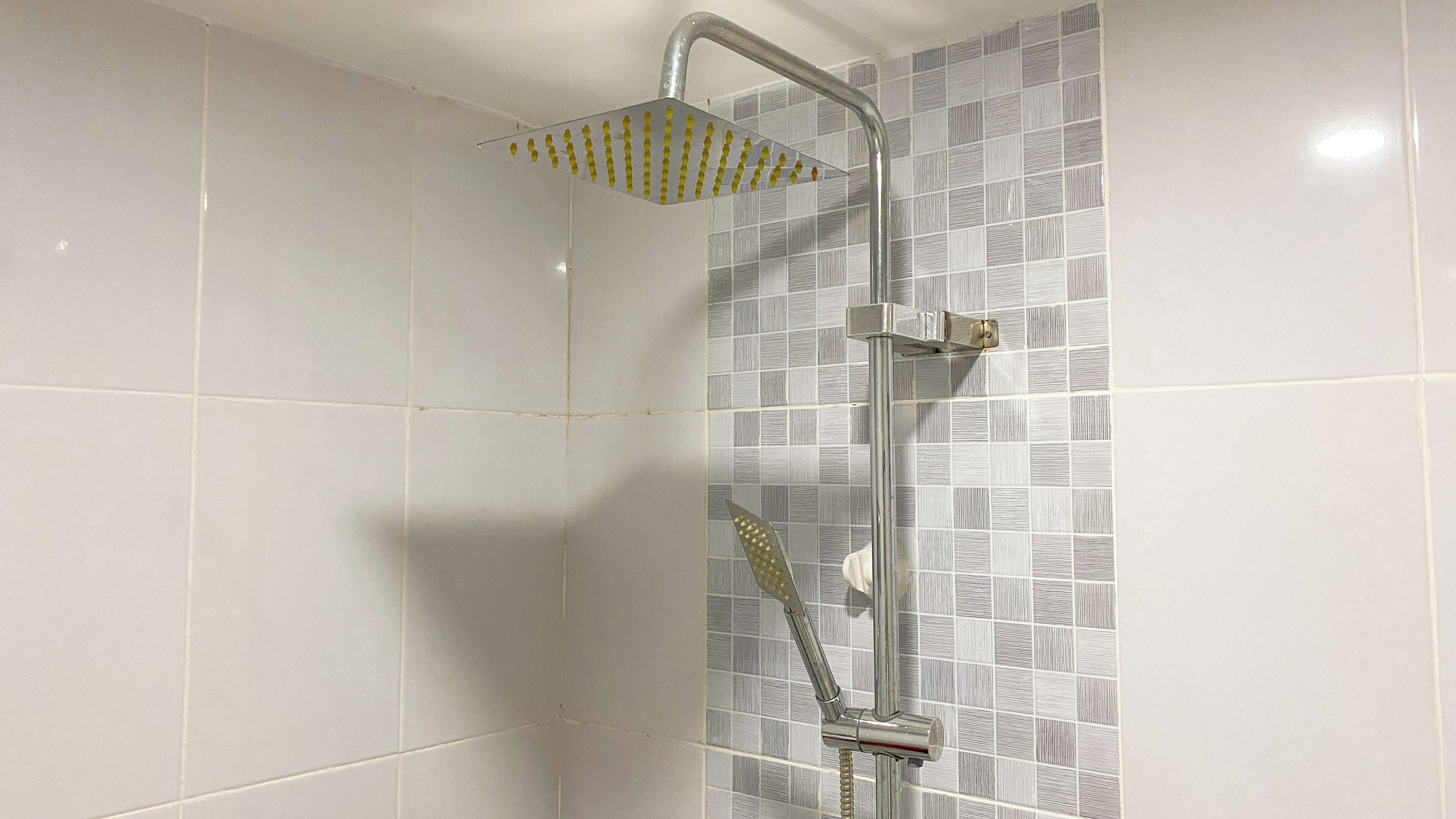 A shower with a rain showerhead and a handheld showerhead, set against a tiled wall with a geometric pattern.
