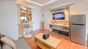 Un salon moderne avec une table basse en bois, un canapé gris et un coin cuisine comprenant un réfrigérateur et un téléviseur.