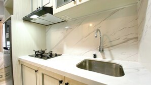 A kitchen with a white marble countertop, a stainless steel sink, a gas stove, and a modern range hood. - Cozy And Best Studio Apartment Tokyo Riverside Pik 2 (Teluknaga)