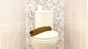 A toilet with a towel on the seat and a showerhead above it. - Cozy And Best Studio Apartment Tokyo Riverside Pik 2 (Teluknaga)