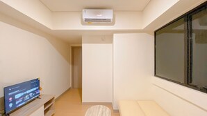 Una stanza con televisore su un supporto in legno, una panca, una finestra e un condizionatore d'aria a soffitto.