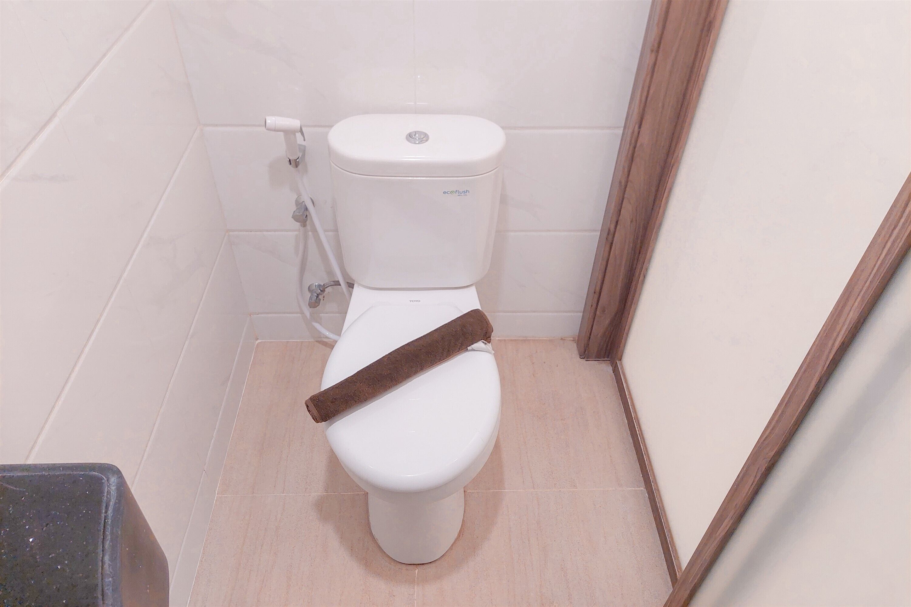 A white toilet with a brown toilet paper holder in a bathroom with white tiles.