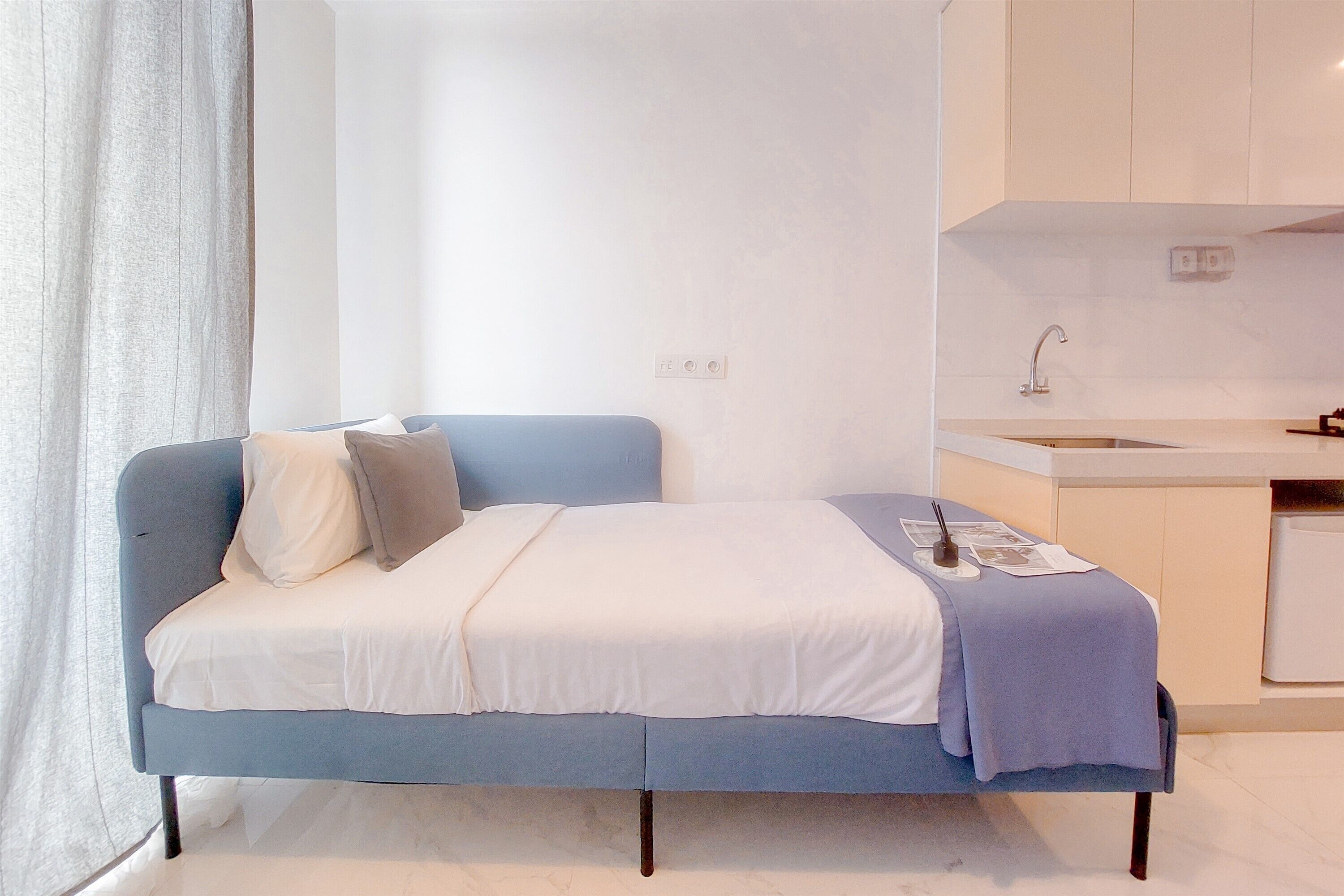 A modern bedroom with a bed, a bedside table, and a built-in kitchen area with a sink and cabinets.