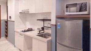 A modern kitchen with white cabinetry, a stainless steel refrigerator, a microwave, and a gas stove. - Good Location And Relaxing 2Br Sky House Bsd Apartment (Pagedangan)