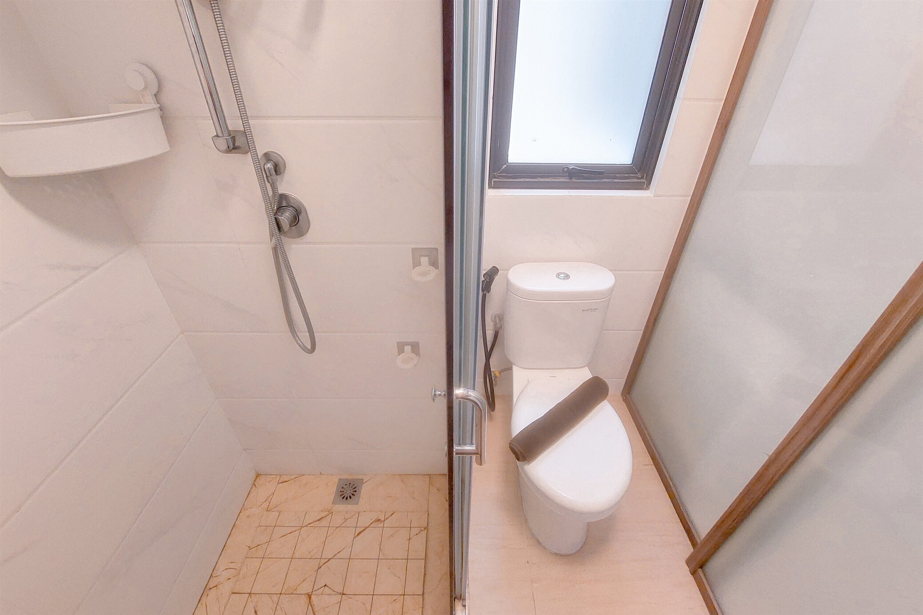 A small, modern bathroom with a glass shower enclosure, a white toilet, and a window providing natural light.