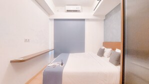 A modern hotel room with a single bed, a nightstand, a shelf, and a ceiling-mounted air conditioner. - Good Location And Relaxing 2Br Sky House Bsd Apartment (Pagedangan)
