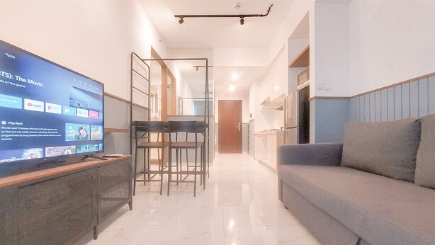 A modern living room with a flat-screen TV, a grey sofa, and a dining area with a table and chairs. - Good Location And Relaxing 2Br Sky House Bsd Apartment (Pagedangan)