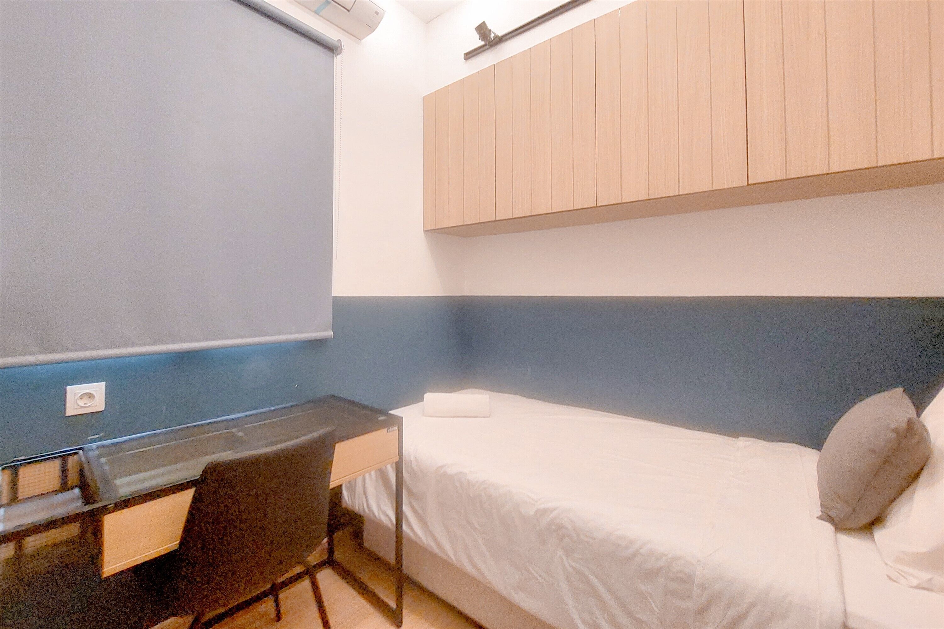 A small, single-bed room with a desk and chair, a wooden wardrobe, and a blue and white wall color scheme.