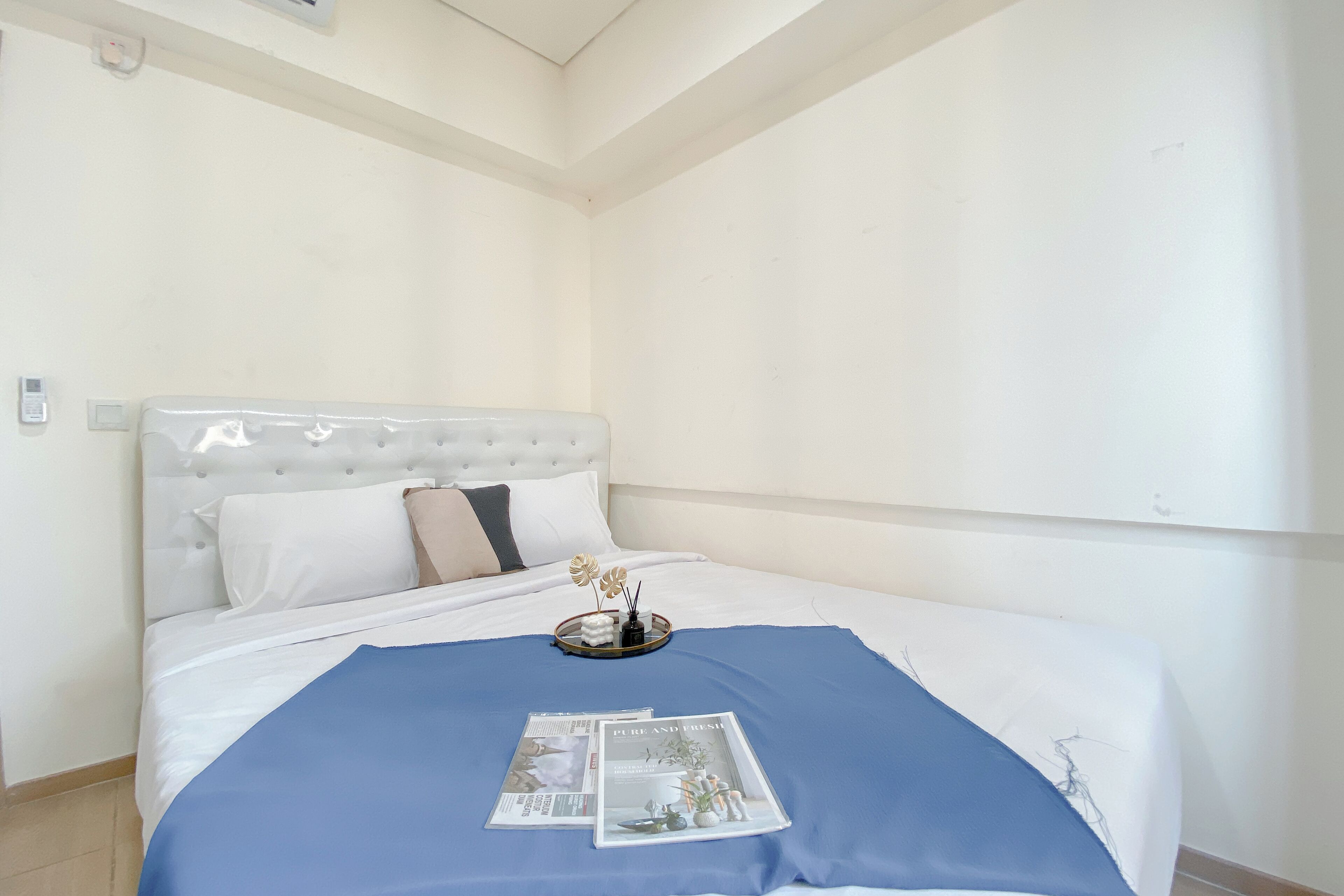 Una cama bien hecha con un edredón azul, una revista y una bandeja con flores.