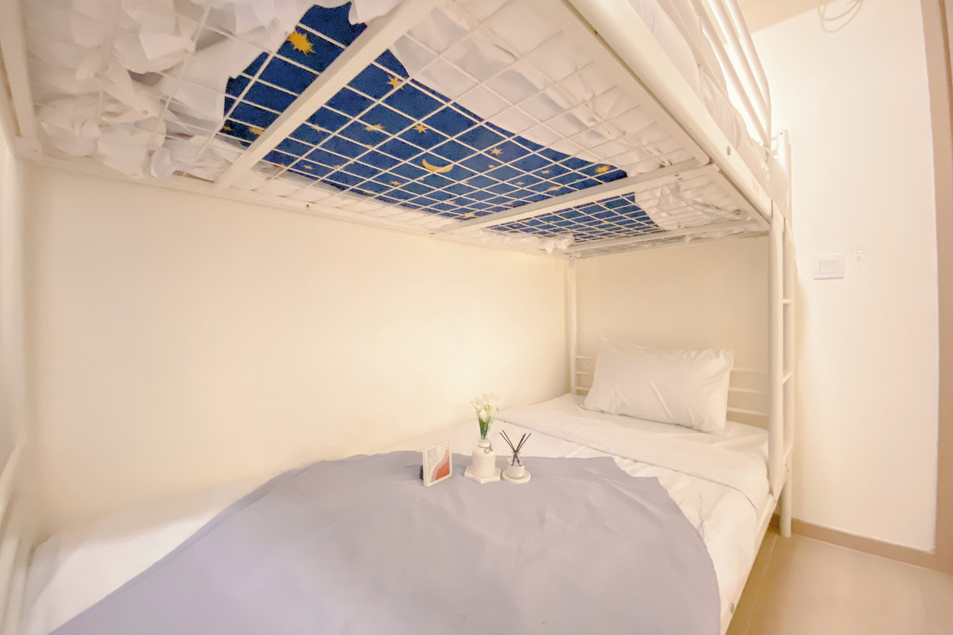 Een stapelbed met een wit frame, een blauw-wit plafond en een klein nachtkastje met een bloevas en een fotolijst.