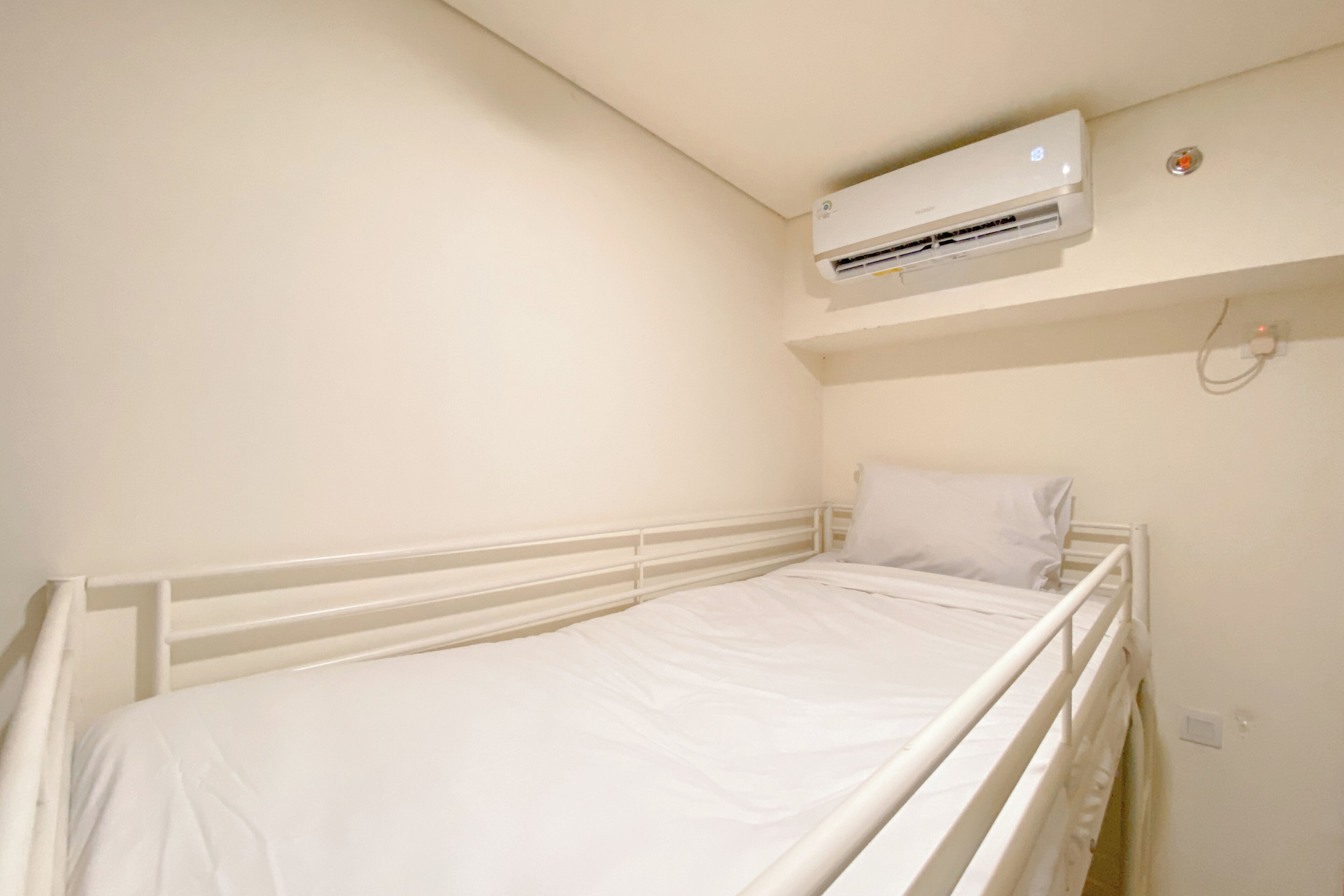 Ein Einzelbett mit weißer Bettwäsche in einem Zimmer mit weißen Wänden und einer darüber angebrachten Klimaanlage.