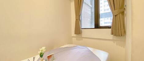 A hotel room with a bed, a window with curtains, and a small table with a vase of flowers and a picture frame.