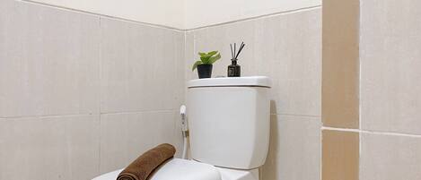 A toilet with a brown towel on the seat and a small potted plant on the tank.