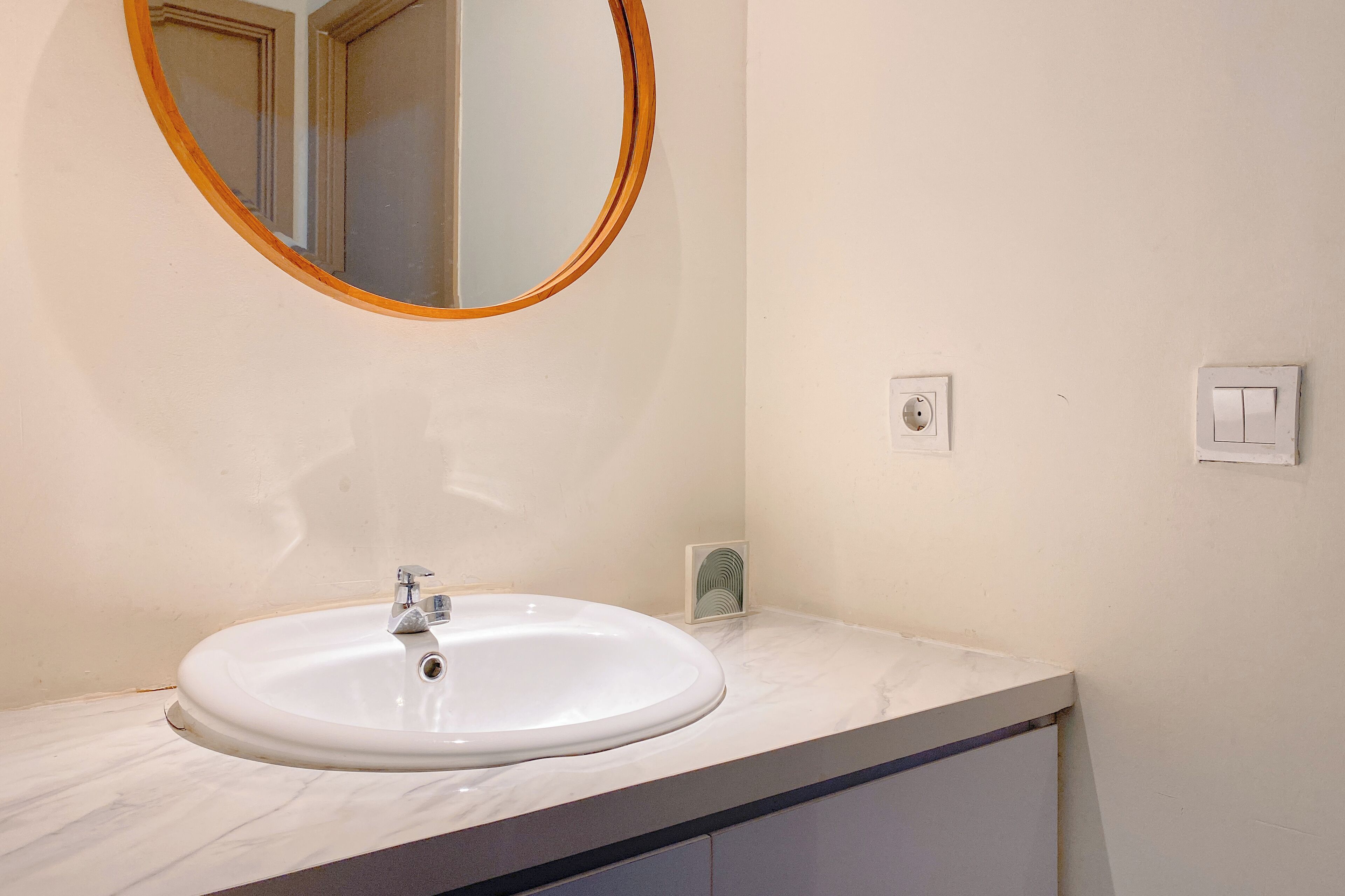 A bathroom with a white sink, a round mirror, and a light switch on the wall.