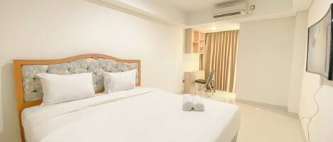 A hotel room with a large bed, a desk, a chair, and an air conditioning unit.