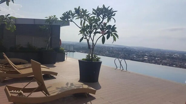 A rooftop terrace with lounge chairs, a potted plant, and a view of a cityscape. - Good And Homey Studio At The Pinnacle Apartment (Semarang)