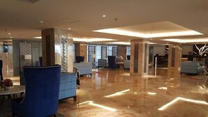 A spacious lobby with a polished marble floor, blue seating, and decorative columns. - Good And Homey Studio At The Pinnacle Apartment (Semarang)