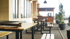 An outdoor seating area with wooden tables and benches, potted plants, and a view of the sea. - The Stylish Studio At Tamansari Panoramic Apartment (Bandung)