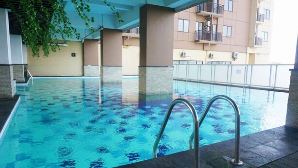 An indoor swimming pool with clear blue water, surrounded by a tiled deck and supported by columns. - The Stylish Studio At Tamansari Panoramic Apartment (Bandung)