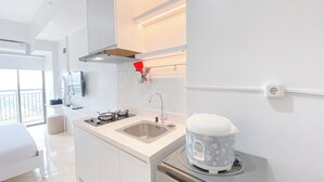 A modern kitchen with a built-in stove, sink, and a compact refrigerator. - The Stylish Studio At Tamansari Panoramic Apartment (Bandung)