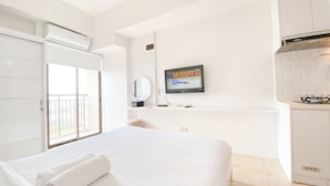 A hotel room with a bed, a TV, a small kitchenette, and a balcony. - The Stylish Studio At Tamansari Panoramic Apartment (Bandung)
