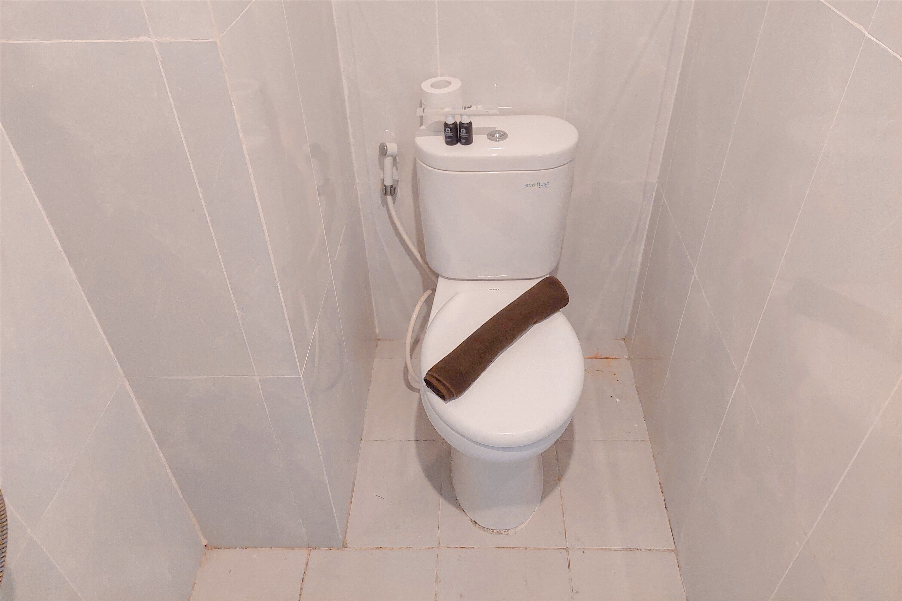 A toilet with a brown toilet paper holder and a roll of toilet paper on the wall.