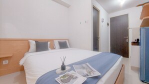 A neatly made bed with a blue blanket, a bedside table with a candle, and two magazines on the bed. - Good Choice And Modern Studio Apartment At Serpong Garden (Cisauk)