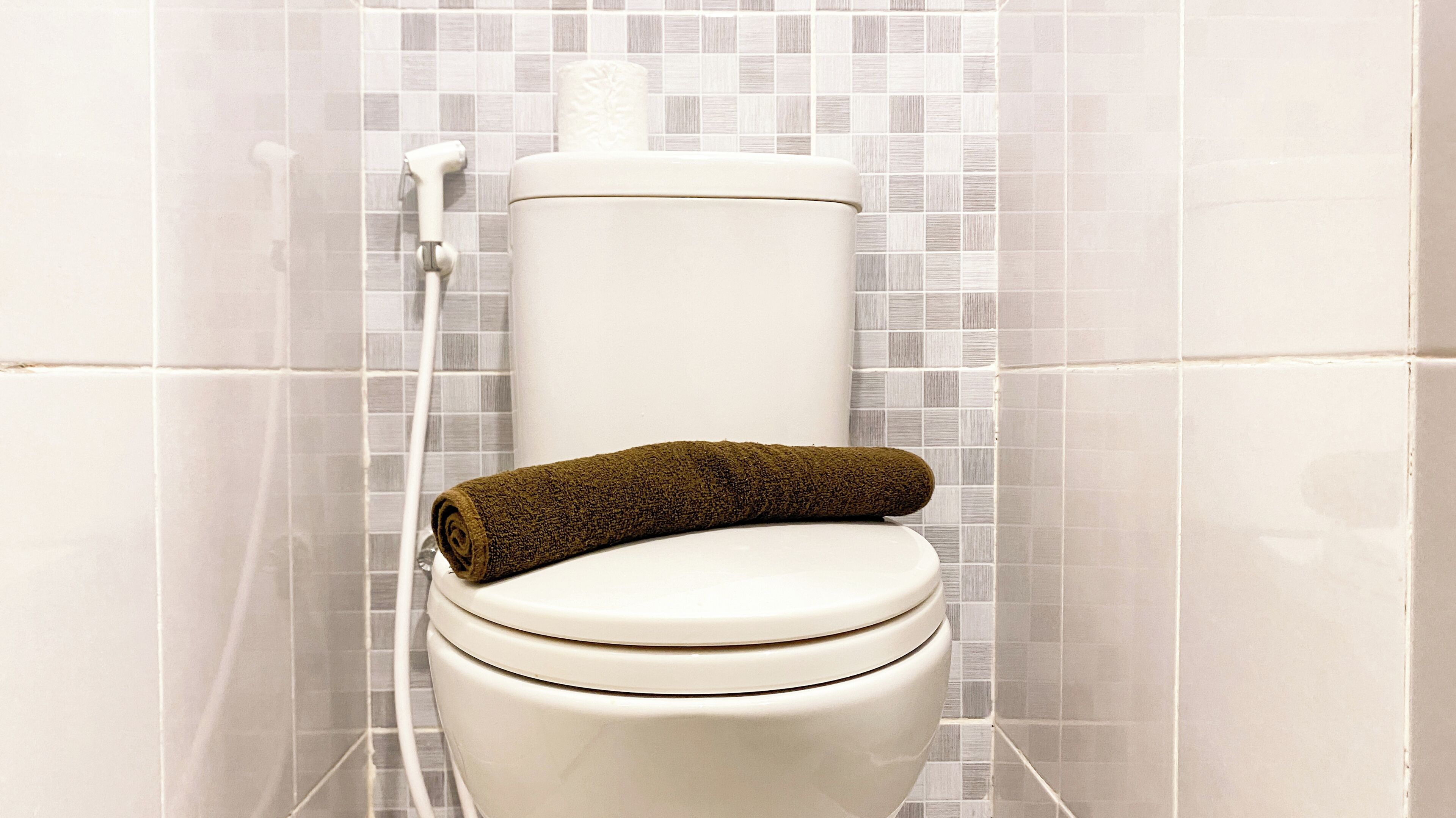Des toilettes avec une serviette sur le siège, un porte-rouleau de papier toilette et un tuyau de douche.