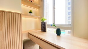 A modern room with a wooden desk, a potted plant, a vase, and a sign listing cities. - Brand New Studio Room At Tokyo Riverside Pik 2 Apartment (Teluknaga)