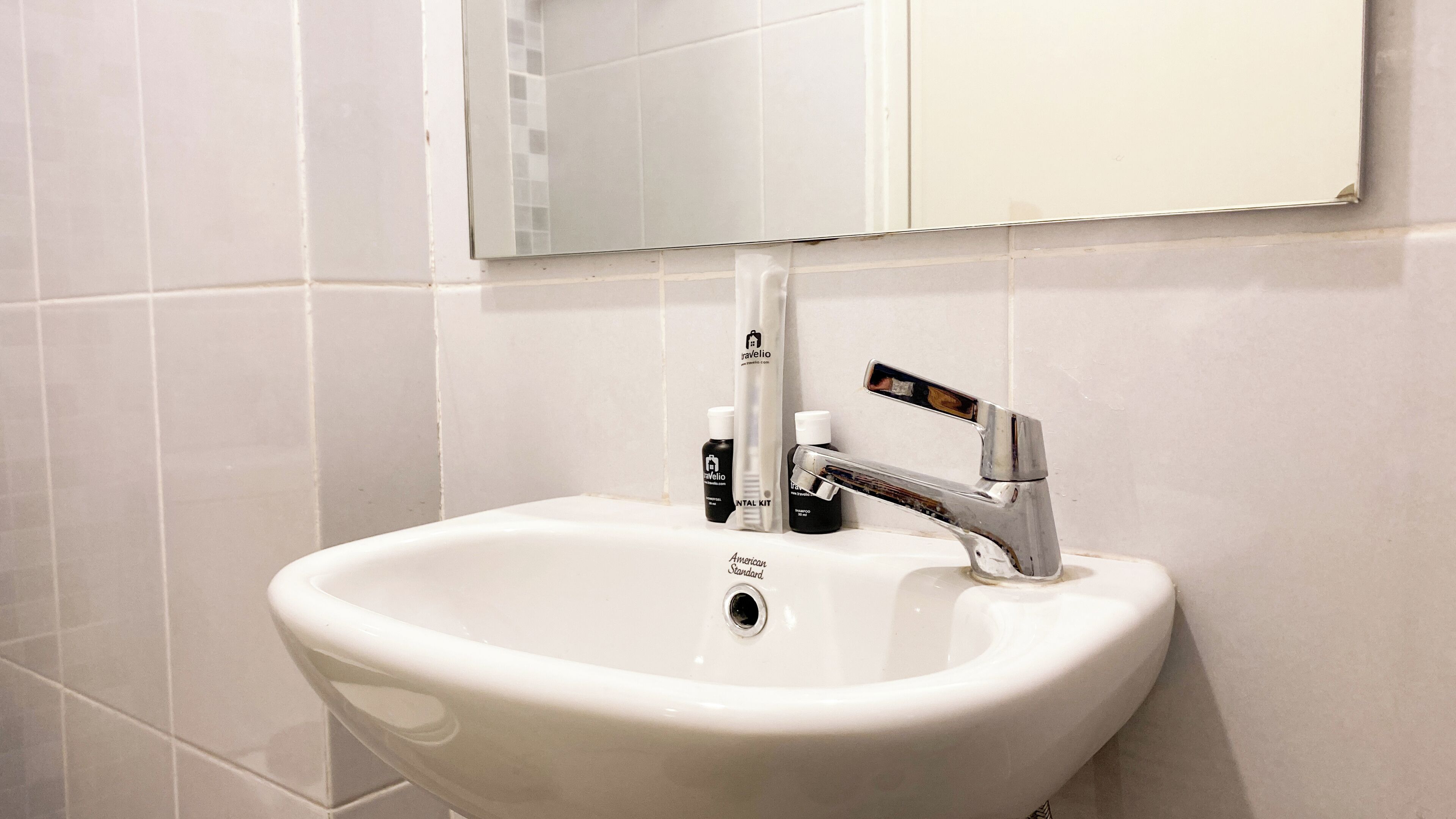 A white bathroom sink with a chrome faucet, a mirror above it, and toiletries on the sink.
