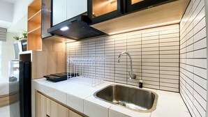 A kitchen with a stainless steel sink, white tiled backsplash, and a black range hood. - Brand New Studio Room At Tokyo Riverside Pik 2 Apartment (Teluknaga)