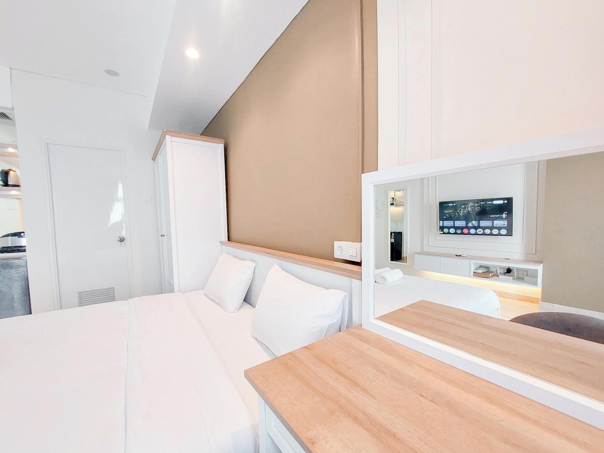 Una habitación de hotel moderna con una cama, una mesita de noche de madera, un televisor montado en la pared y un espejo sobre la mesita.