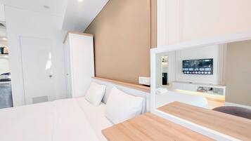 Una habitación de hotel moderna con una cama, una mesita de noche de madera, un televisor montado en la pared y un espejo sobre la mesita.