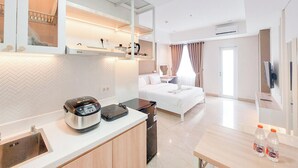 A modern hotel room with a kitchenette, a bed, a desk, and a bathroom. - Comfortable Studio At Podomoro City Deli Medan Apartment (Medan)