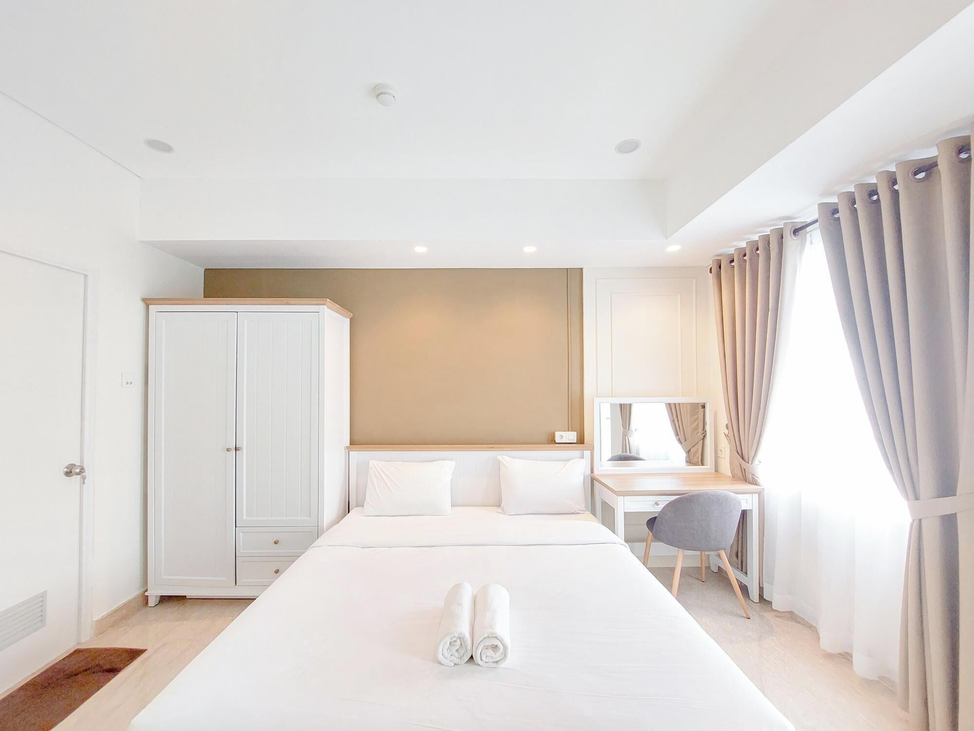 A hotel room with a large bed, a desk, a wardrobe, and a window with curtains.