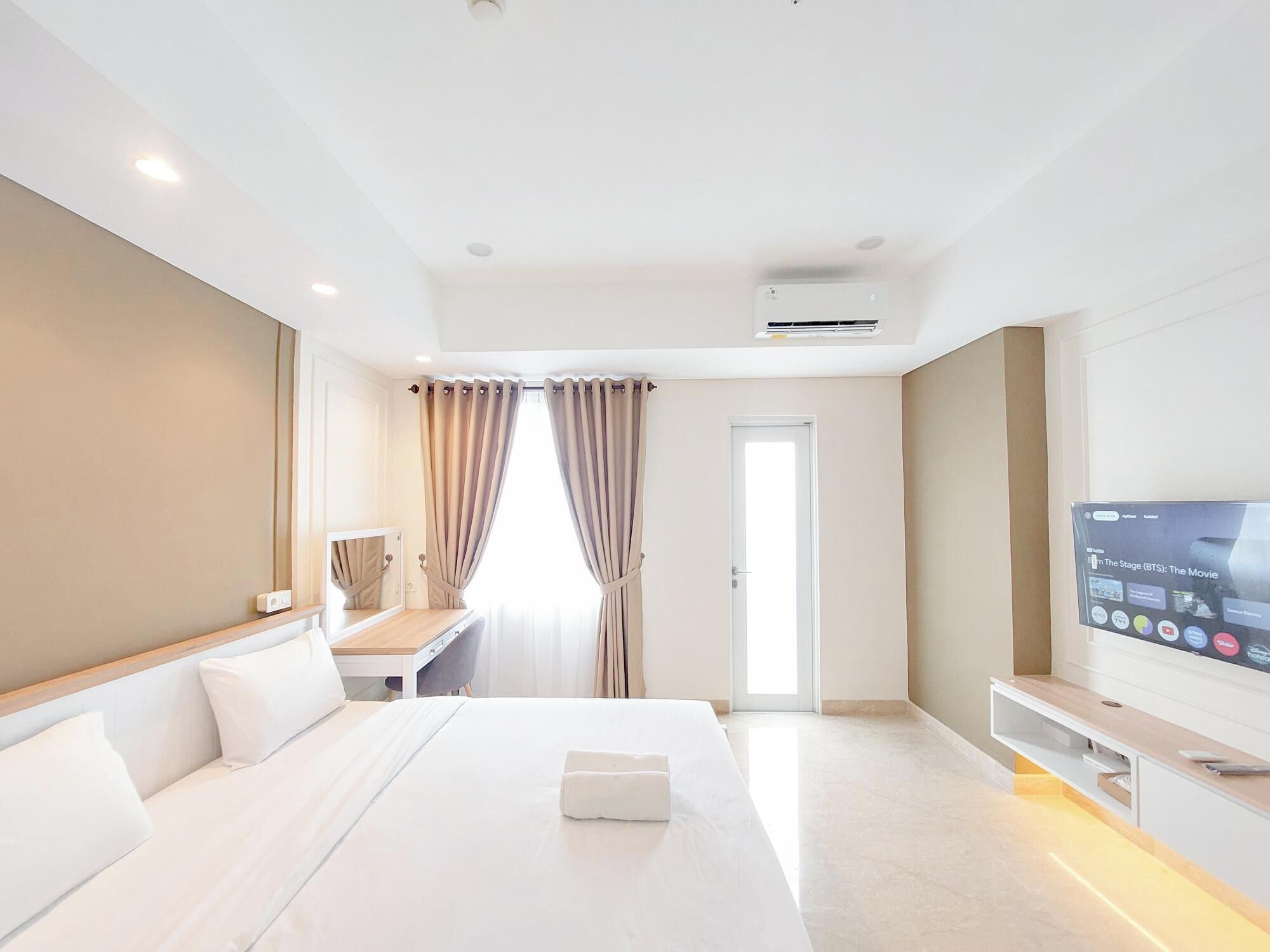 A modern hotel room with a bed, a desk, a TV, and a door.