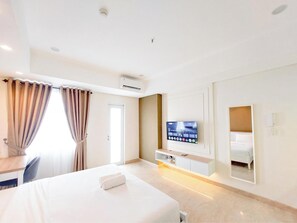 A hotel room with a bed, a TV mounted on the wall, a mirror, and a window with curtains. - Comfortable Studio At Podomoro City Deli Medan Apartment (Medan)