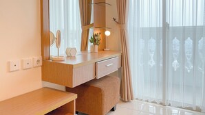 Une chambre moderne avec une coiffeuse en bois, un miroir, une table de chevet et une grande fenêtre ornée de rideaux légers.