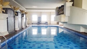 Une vaste piscine intérieure dotée d’un sol et de murs carrelés, flanquée de colonnes et agrémentée d’éléments décoratifs.