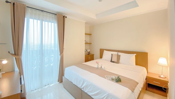 Une chambre d’hôtel avec un grand lit, une table de chevet, une commode, une fenêtre avec des rideaux et un luminaire au plafond.