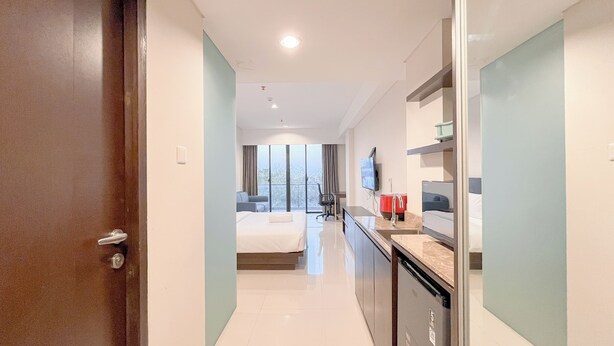 A modern hotel room with a bed, a desk, a sink, and a large window. - Studio Near Nusa Dua Convention Center Bali at Skales Residence (Nusa Dua)