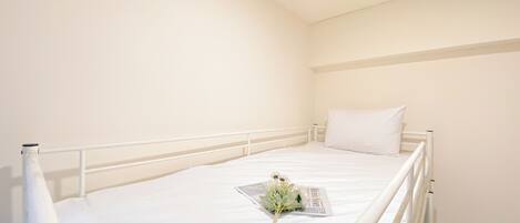 A single-bed room with a white mattress, a white headboard, and a white pillow.