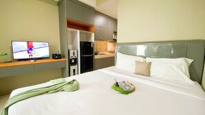A hotel room with a bed, a television, a minibar, and a kitchenette. - Warm And Cozy Living Studio Apartment At B Residence (Pagedangan)