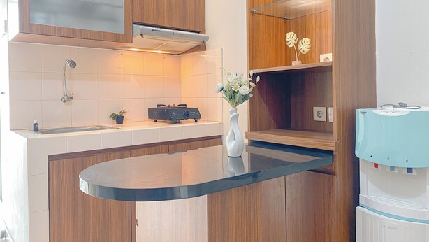 A modern kitchen with wooden cabinets, a black countertop, a built-in stove, and a water dispenser. - Good And Homey 2Br At Apartment Green Palm Residence (Jakarta)