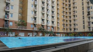 A swimming pool surrounded by a high-rise residential building with balconies. - Good And Homey 2Br At Apartment Green Palm Residence (Jakarta)