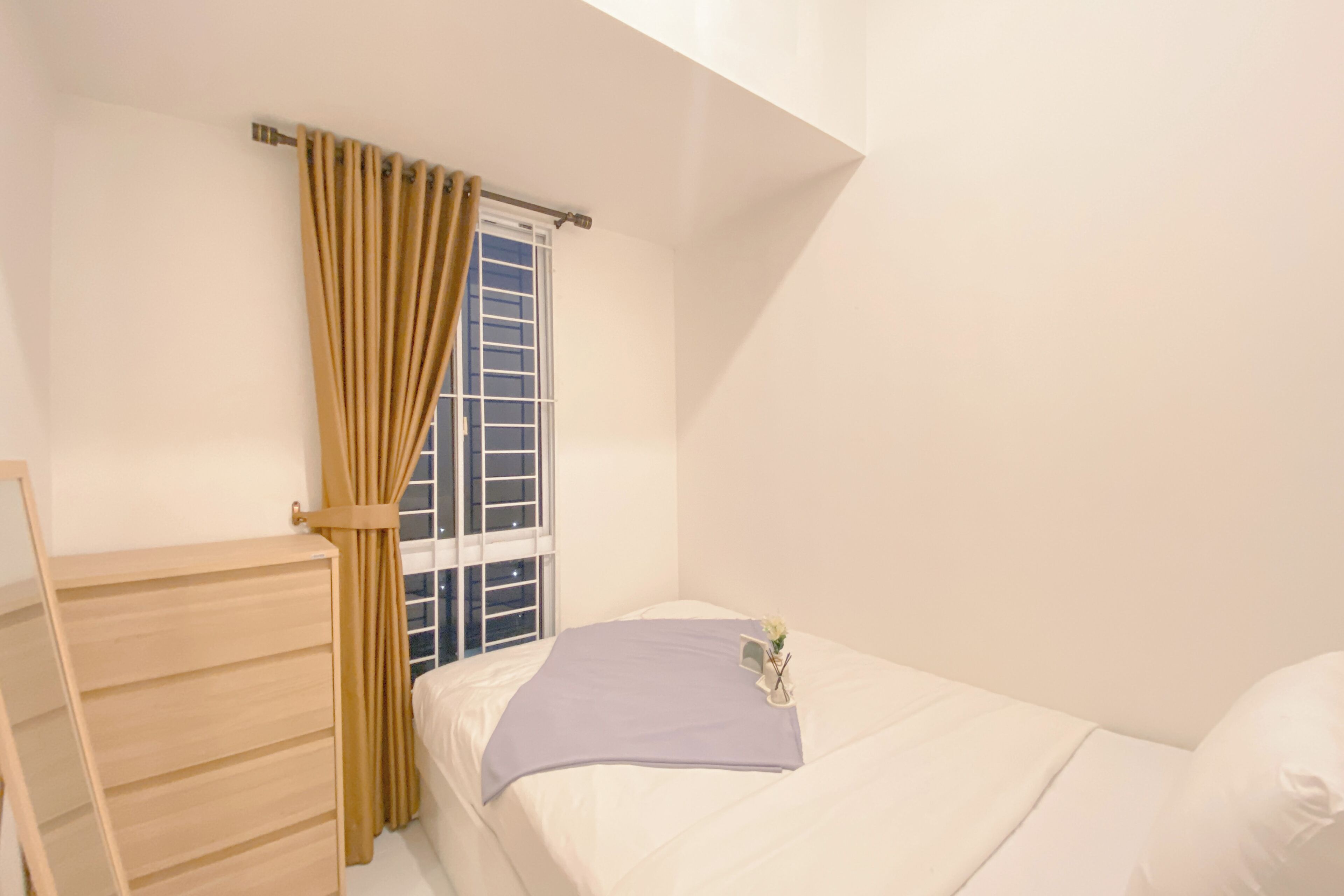 A bedroom with a single bed, a wooden dresser, and a window with curtains.