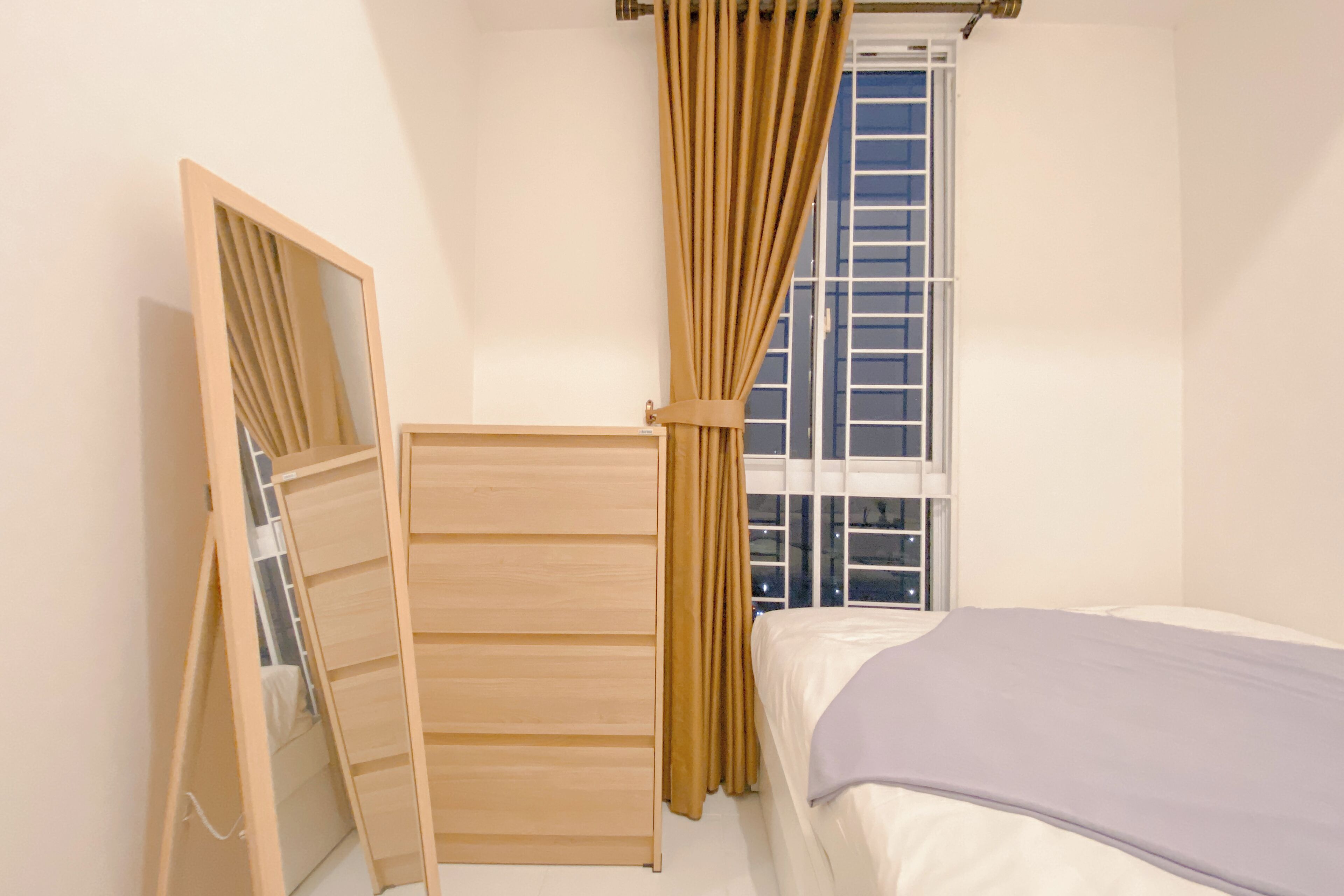 Une chambre à coucher avec un lit, une armoire en bois, un miroir et une fenêtre avec des rideaux.